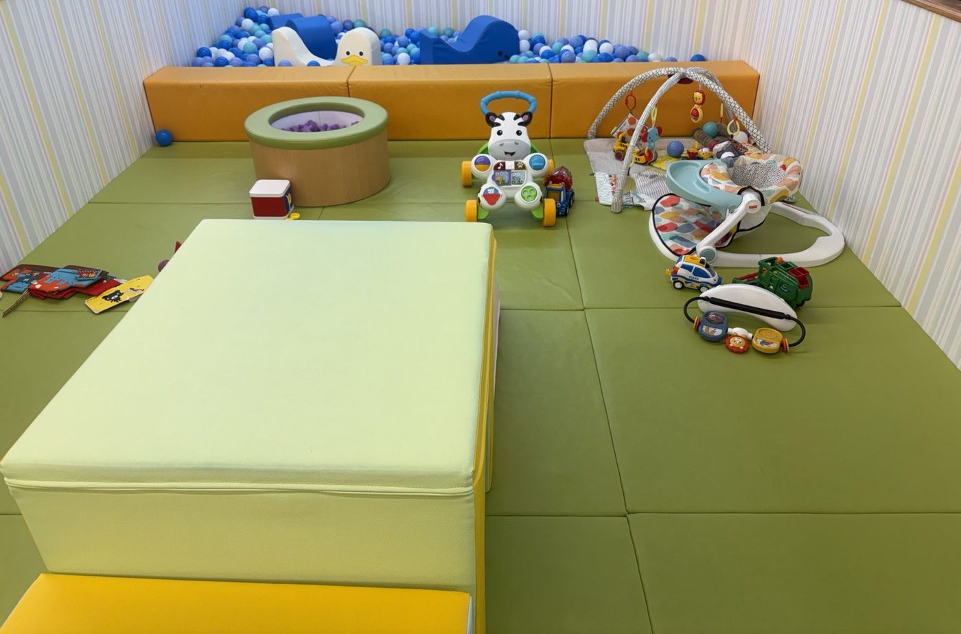 ピュアハートキッズランド ポンテポルタ千住店のベビーパーク。マットを敷いた区画に小さなボールプール、手押し車のおもちゃ、簡易的な滑り台、ベビージムが置かれている