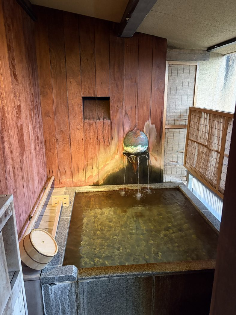 客室の露天風呂。石の四角い湯船に、壁の湯口から源泉が注いでいる。横に木の手桶